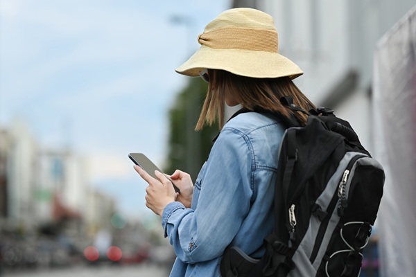 Frau mit Rucksack und Hut schaut auf ihr Smartphone, während sie durch die Stadt läuft.